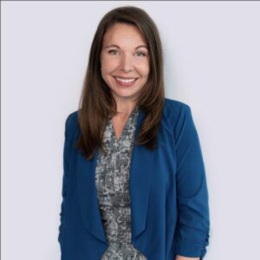 Brown haired woman wearing blue blazer smiles into camera 