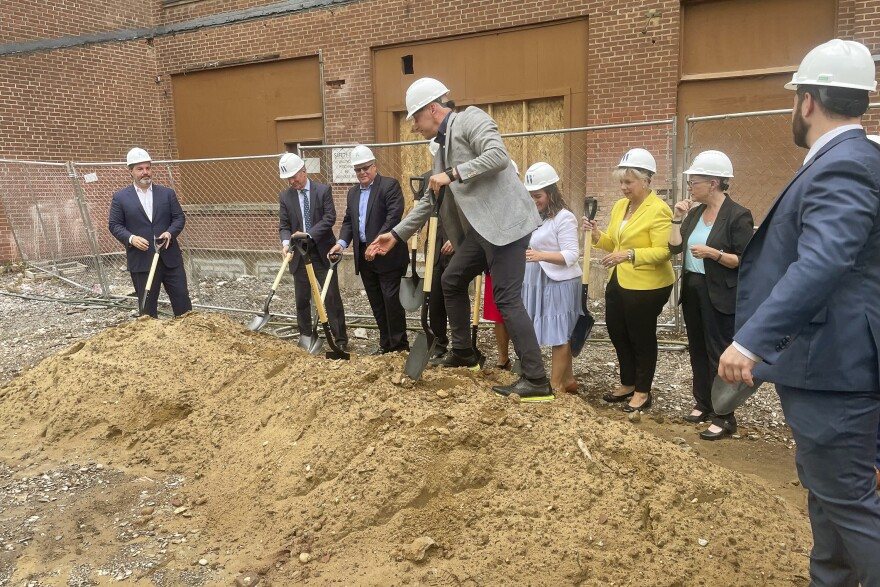 Pat Guliano, managing director of multifamily for CHFA, scales a mound of dirt during groundbreaking ceremonies for a $55 million project to develop the Landers, Frary & Clark factories into a 154-unit apartment and affordable housing community.