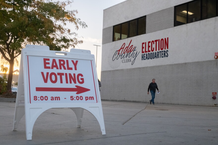 A man walks in front of a beige building near a sign indicating early voting is underway.