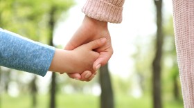 Little child holding hands with his mother outdoors, closeup. Family time