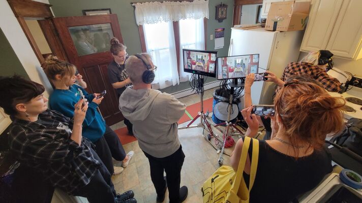 A film crew standing around a couple monitors in a kitchen.