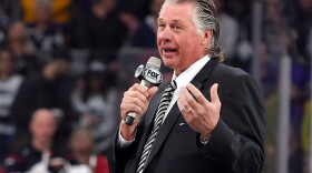   Barry Melrose speaks to fans holding a microphone at an arena