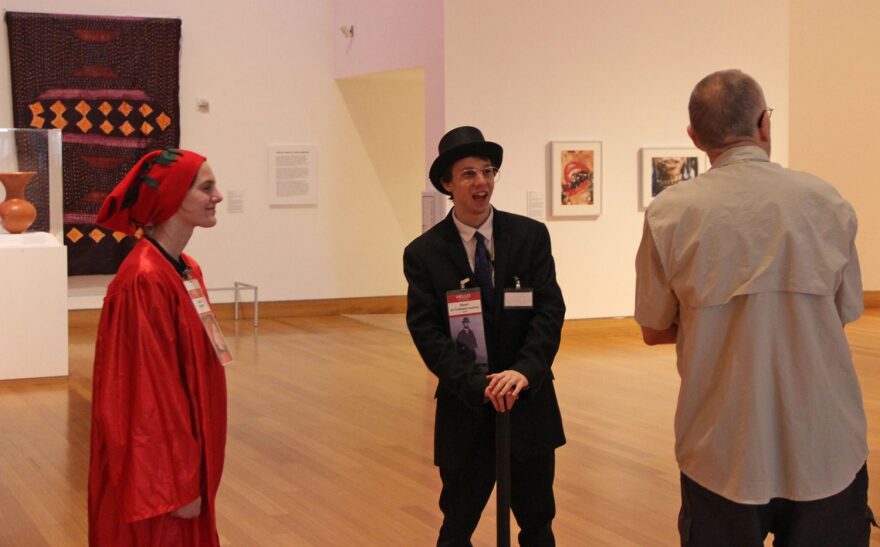 Daireen Espinosa (left) and Jason Wilkotz (center) entertain a visitor while telling him facts about Dante Alighieri and Henri de Toulouse-Lautrec. Both Espinosa and Wilkotz are dressed as Alighieri and Toulouse-Lautrec respectively. (Jose Sanchez/WUFT News)