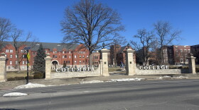 Patches of snow cover the ground in front of the gates of Columbia College on a sunny winter day. The word "Columbia" sits on the left gate and "College" on the right with a sidewalk in the middle. 