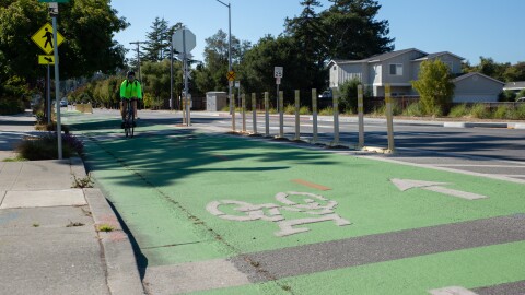 A cyclist bikes in a protected bike lane, which has dividers between the path and the main road.