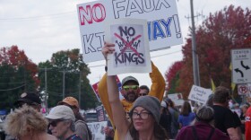 Protestors hold up signs during the "No Kings 2.0" Protest along Drake Road in Kalamazoo on Saturday, Oct. 18. In the foreground, a woman holds a small sign saying "No Kings". A sign in the back reads "No Faux-King way".