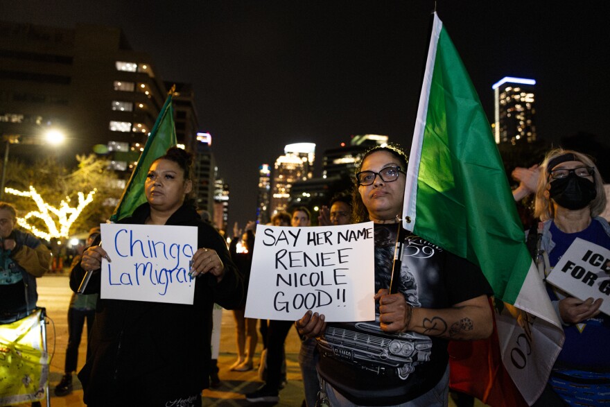 Two women hold Mexico flags and signs, one of which reads "Say her name, Renee Good", the other sign reading "Chinga la Migra" at a protest held at night. 
