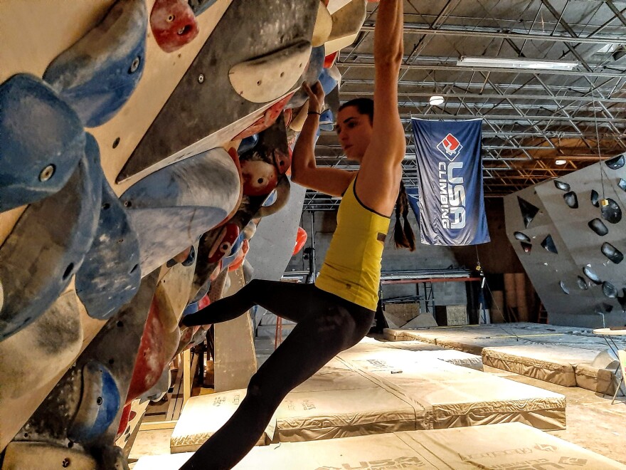 A woman hangs off of colorful plastic holds on a steep wall.