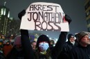 A protester holds a sign reading "ARREST JONATHAN ROSS" during a rally for Renee Good, Thursday, Jan. 8, 2026, in Minneapolis, after she was fatally shot the day before.