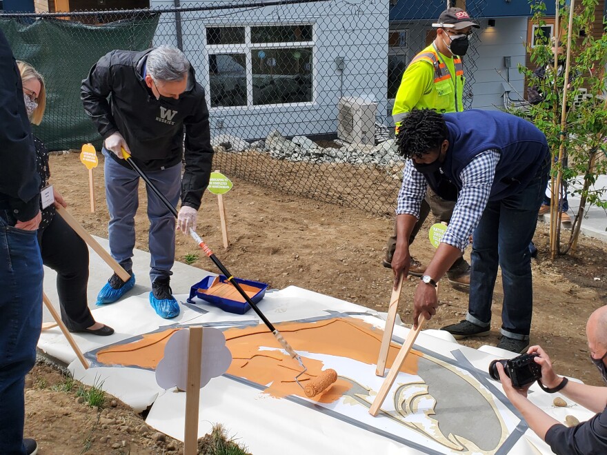 King County Executive Dow Constantine, at left in UW mask, helps paint a design on the sidewalk at Willowcrest.