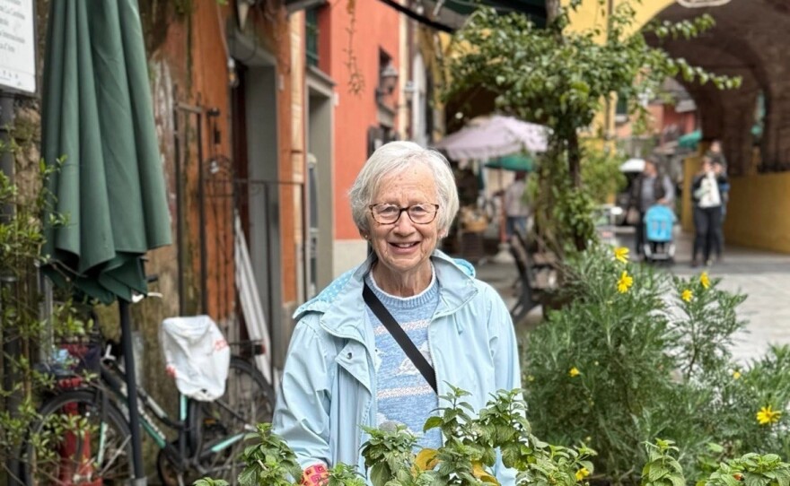 A woman with short grey hair stands in the middle of many buckets of flowers.