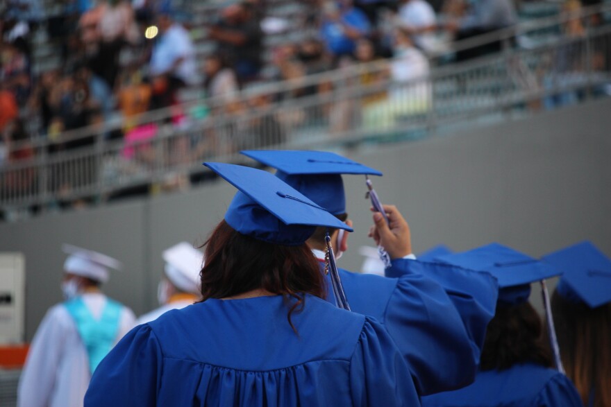 Teenagers walking away wearing blue caps and gowns.