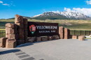 The Yellowstone National Park sign in front of large snow capped mountains.