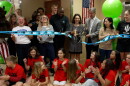 A group of elementary students watch as a ribbon is cut.