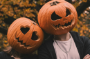 Two people with pumpkins on their heads with pumpkin carvings in a smile