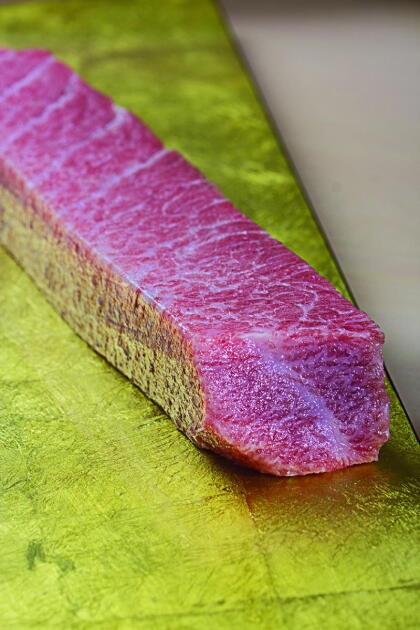 A thick block of marbled fatty tuna belly resting on a gold surface, the kind of premium cut featured in Yui Edomae Sushi omakase dinners