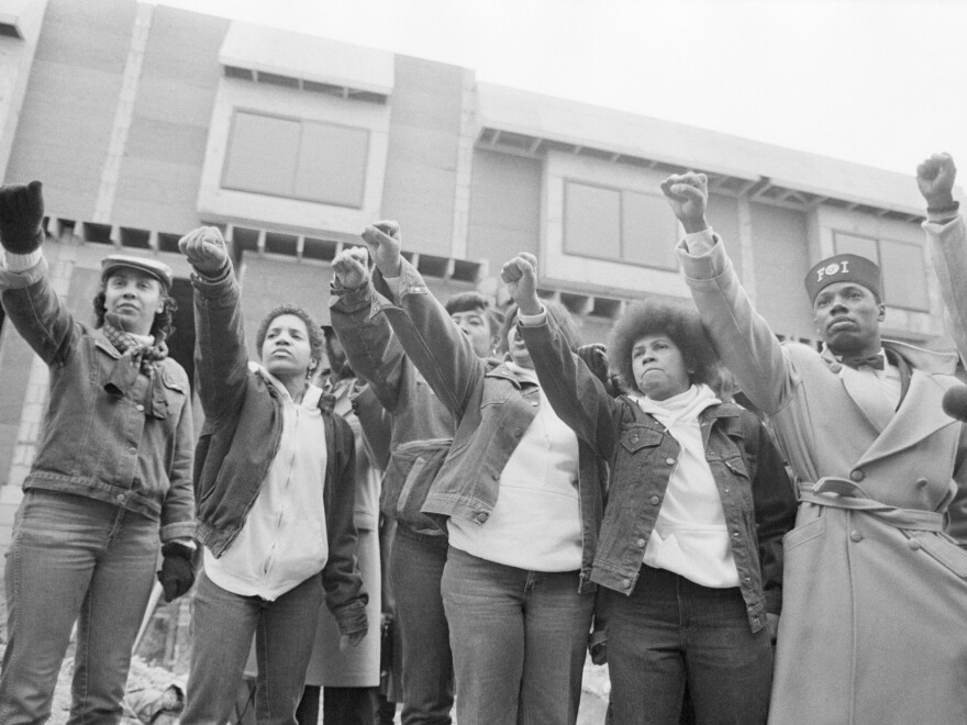 Mourners of MOVE members killed in the bombing by the Philadelphia Police stand in front of their former headquarters. They raise their arms with the Black Power salute as the funeral procession for leader John Africa passes.