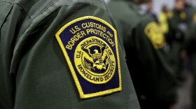 A yellow trimmed dark blue patch sits on a dark green sleeve. Encircling the top of the yellow U.S. Department of Homeland Security is the agency title of U.S. Customs and Border Protection. 