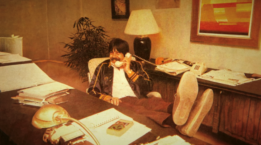 Throwback photo of David Marsden at a desk with his feet up, talking on a landline phone.