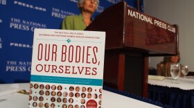 Judy Norsigian, executive director and founder of Our Bodies, Ourselves, speaks behind a copy of the women's health guide at the National Press Club in 2012.