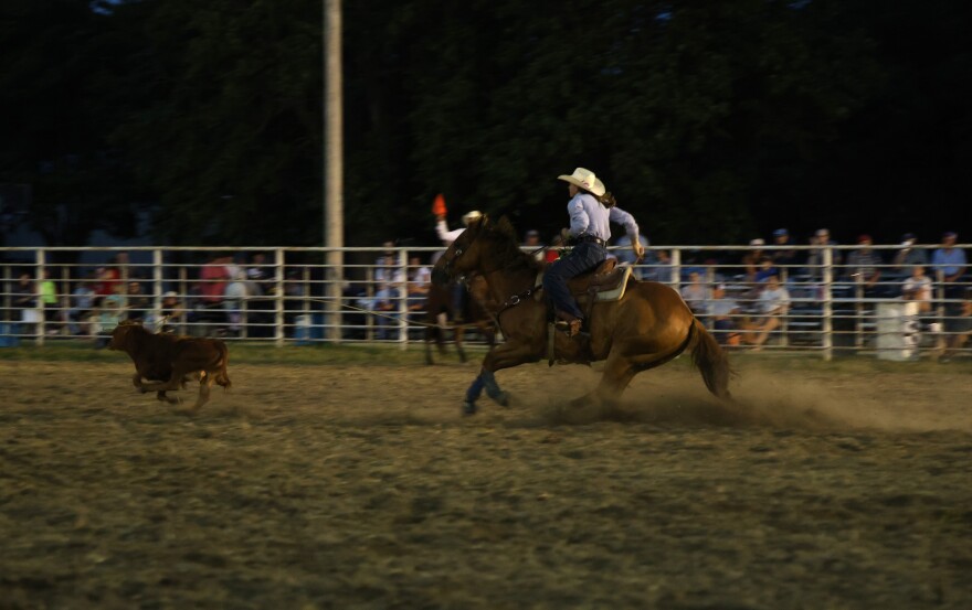 Rachel Brownback competes in the breakaway roping at the Hepler Ruritan Club Rodeo. She's on her horse, chasing after a calf. She's thrown her rope, which is mid air above the calf's head.