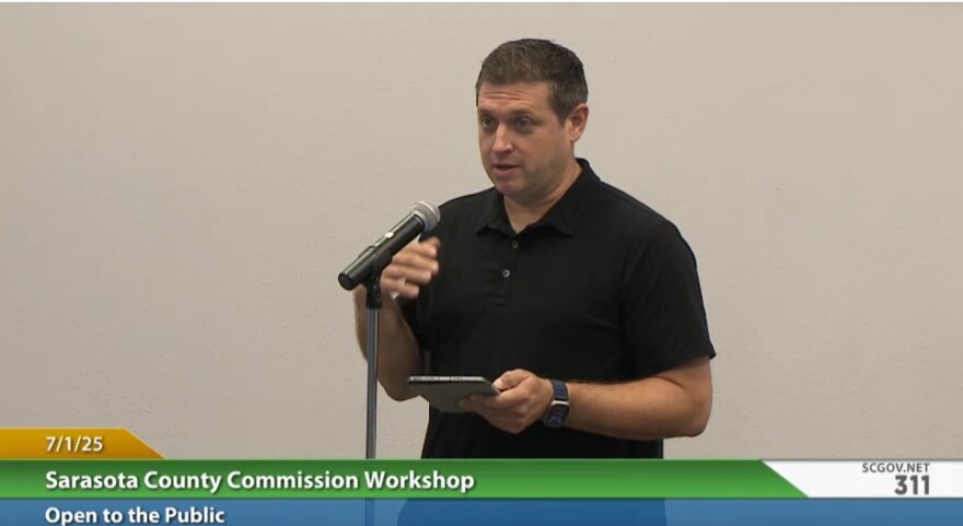 A man in a black short sleeved shirt speaks at a podium