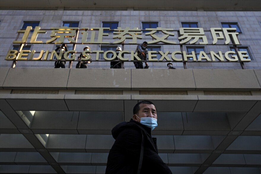 A man wearing a face mask looks back as workers install the nameplate of the Beijing Stock Exchange on Financial Street in Beijing, Sunday, Nov. 14, 2021. (AP Photo/Andy Wong)
