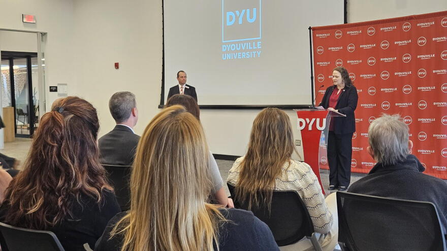 Shannon Mcrory-Churchill, dean of D'Youville University's PAtricia H. Garmon School of Nursing, stands at a lectern describing the impact of $3 million in federal grant money.