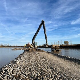 A dump truck and an excavator unload sand on a stony barrier island in the Sandusky Bay.