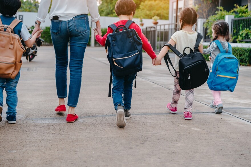 Back of Mother and kids holding hands walking to school