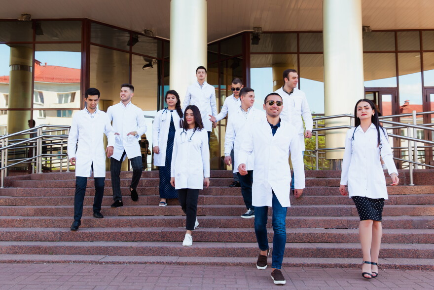 A friendship group of European medical students presented outdoor against the university door on the steps.