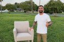 Man in white t-shirt stands outside next to a chair 