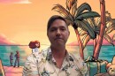 Man wearing a Hawaiian shirt with a graphic of the beach and people on it behind him 