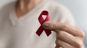 A hand holds up a red ribbon as an HIV or AIDS awareness symbol