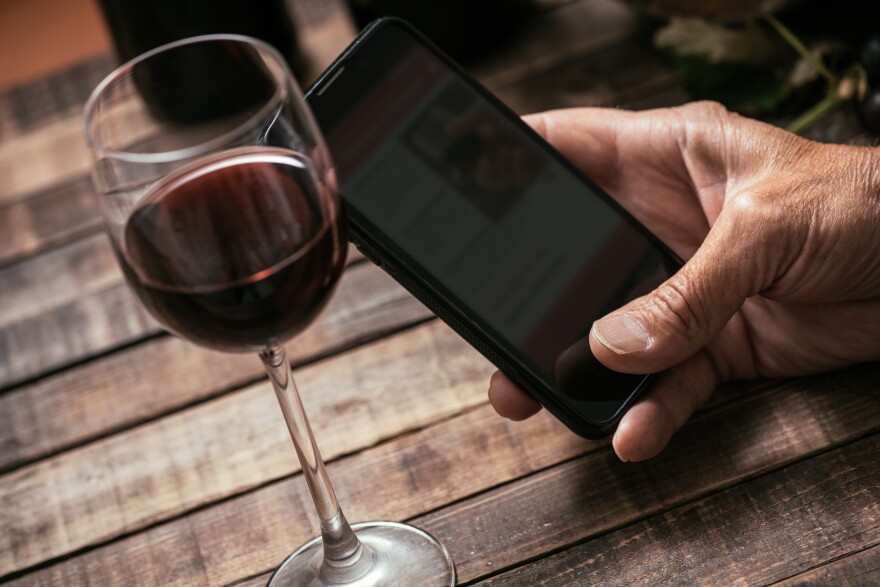 A glass of wine with an iphone next to it, on a wooden tabletop.