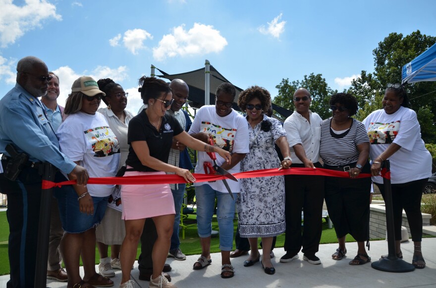 A group of people stand behind a red ribbon. A woman with scissors cuts the ribbon.
