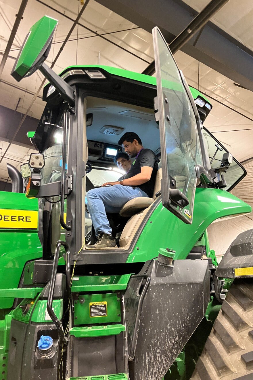 Students sits in the cab of a green tractor.