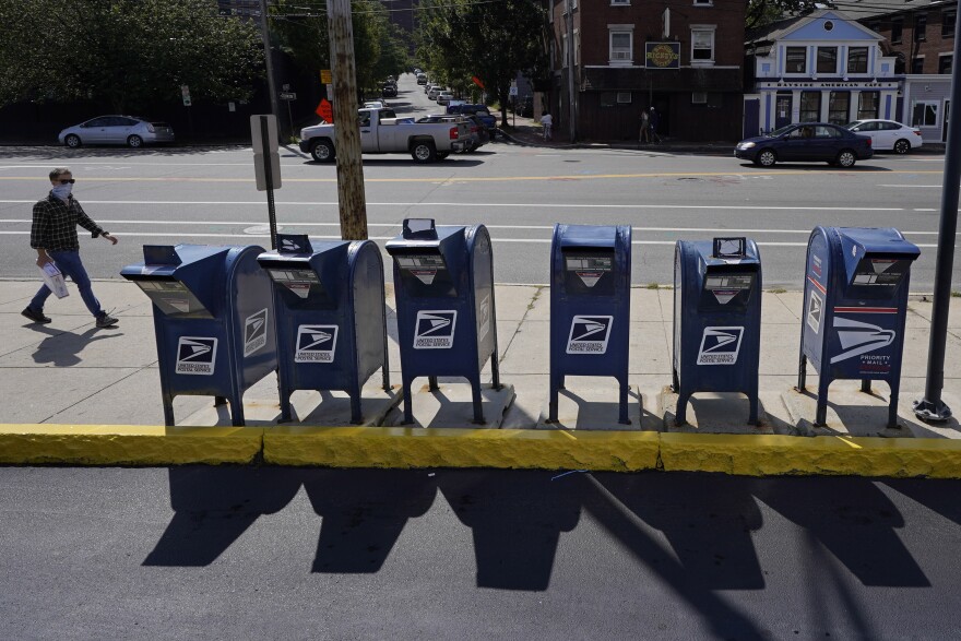 A man walks by a row of U.S. Postal Service mailboxes on his way to the post office, Tuesday, Aug. 18, 2020, in Portland, Maine.