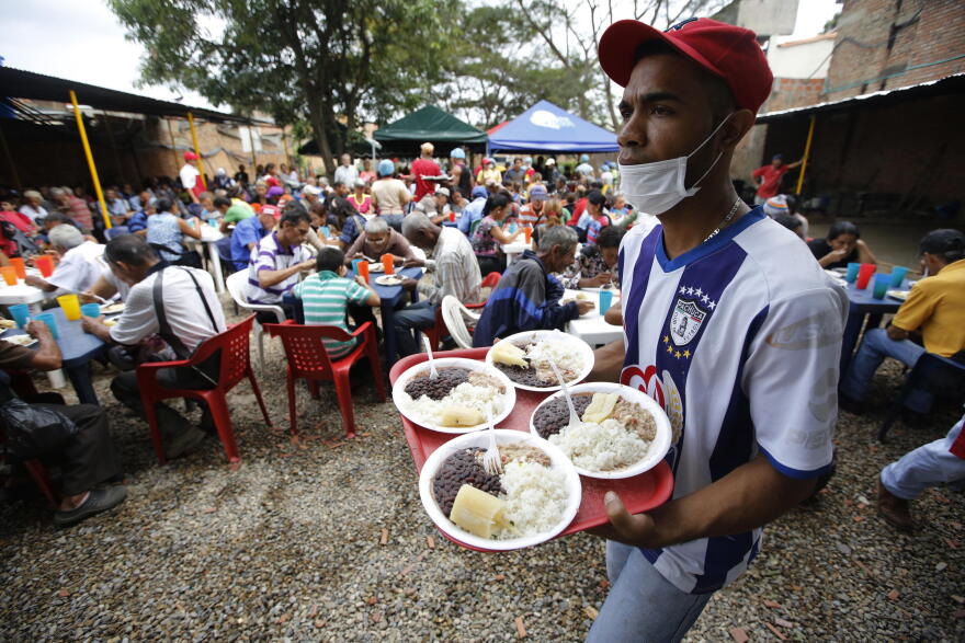In this Feb. 23, 2018 photo, a volunteer at the "Divina Providencia" migrant shelter distributes lunch to Venezuelan migrants, in Cucuta, Colombia. The food is cooked in several large vats and the diocese says it offers an average of 1000 meals a day.