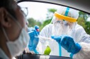 Stock image of a medical worker administering a COVID-19 test through the window of a vehicle