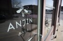 Outdoor photo showing the exterior door of a restaurant on a sunny day. The signage on the door shows a stylized bee with the word "Anjin" printed below it.