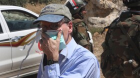 In this photo taken during a government-organized tour for  foreign diplomats and the media, US ambassador to Syria Robert Ford covers his nose from the smell of the dead bodies during his visit with other foreign diplomats to a mass grave, in Jisr el-Shughour, north of Syria, on Monday, June 20, 2011.
