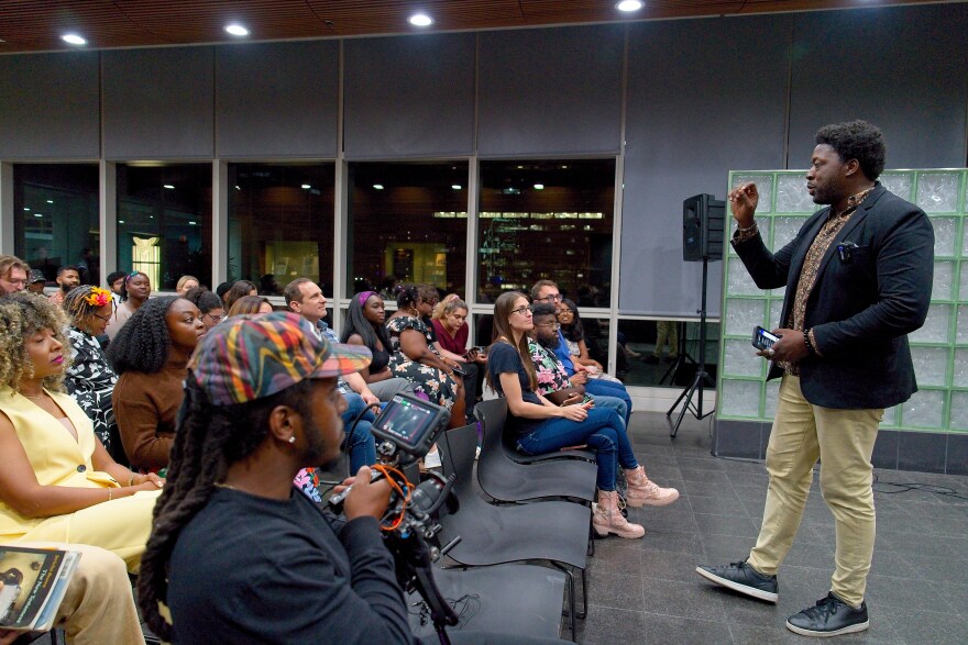 A man on the left speaks to a seated crowd 