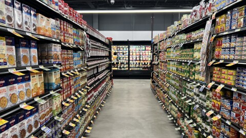 Two shelves are lined to the edge with canned goods, leading down an aisle to coolers at Gettysburg Grocery