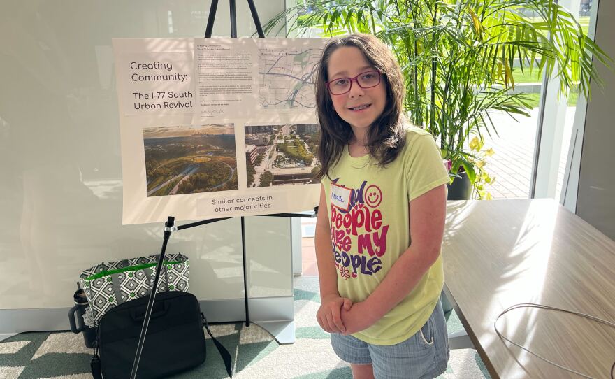 A student stands next to her design concept for Interstate 77.