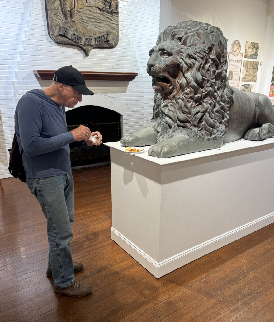 A visitor to the Matheson History Museum's “The Alachua Phenomenon” exhibition enjoys refreshments next to a bronze lion sculpture once stationed at the Alachua County Courthouse in 1885. (Preston Allen/WUFT News)
