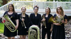 The members of the Coda Brass Quintet, dressed in concert black and holding their instruments.
