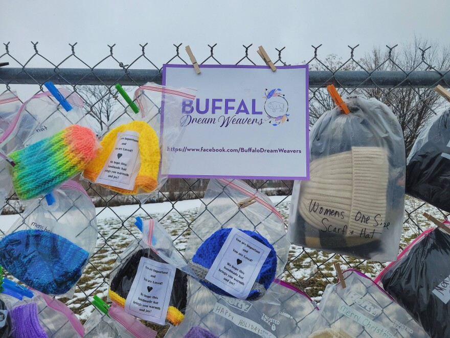 Bagged articles of clothing attached to a chain link fence with a sign for Buffalo Dream Weavers