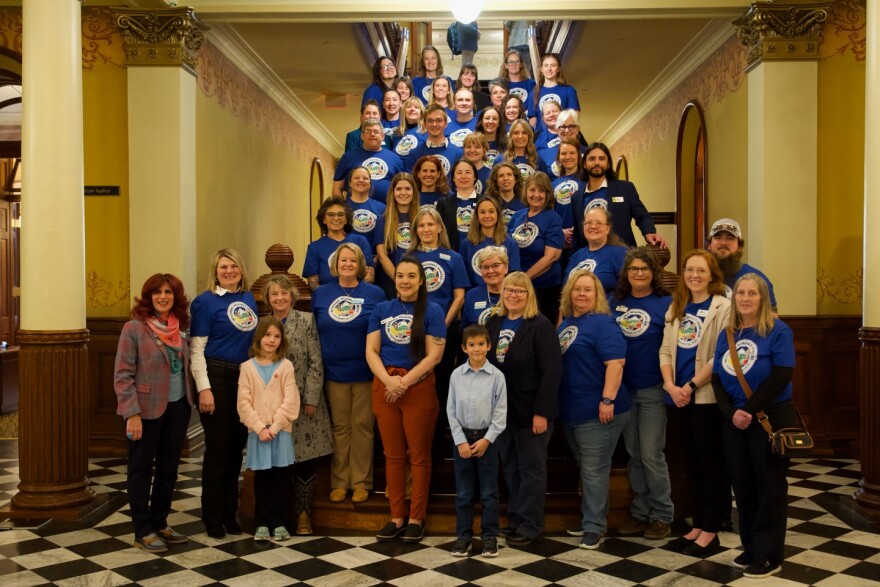 A large group of people in matching t-shirts stand on the stairs in the Wyoming Capitol.