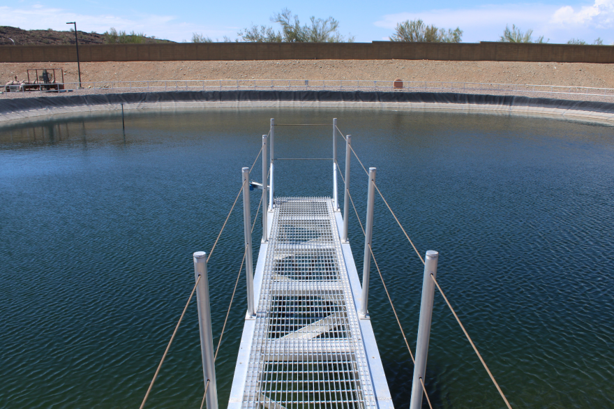 A metal dock with railings on all sides stretches out into a seemingly man-made pond.